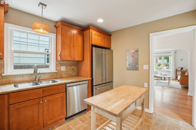 6134 NE 25th Ave, Portland, OR 97211 - kitchen with stainless steel appliances, a sink, brown cabinetry, decorative light fixtures, and backsplash