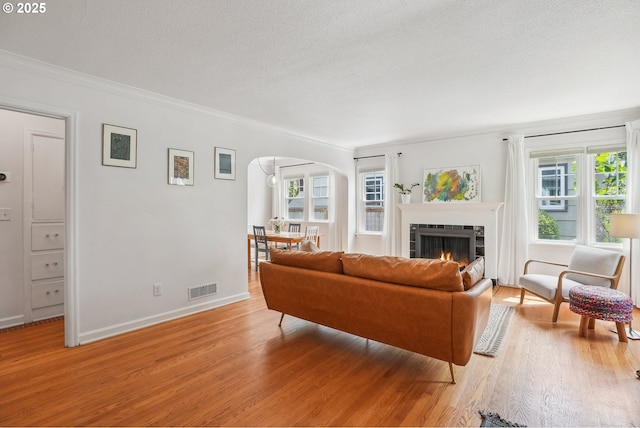6134 NE 25th Ave, Portland, OR 97211 - living room featuring light wood-type flooring, arched walkways, a textured ceiling, ornamental molding, and a tiled fireplace