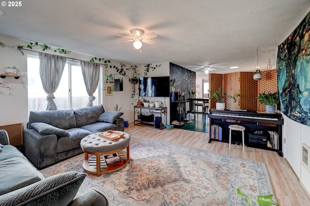 living room featuring ceiling fan, a textured ceiling, and light wood-type flooring