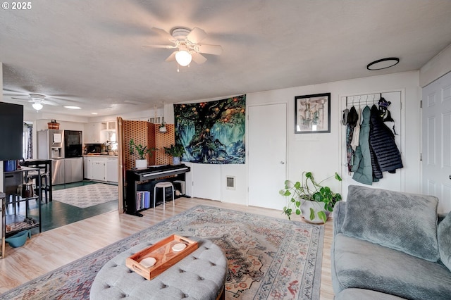 living room with a textured ceiling, ceiling fan, and light hardwood / wood-style flooring