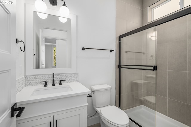 bathroom featuring tasteful backsplash, vanity, toilet, and a shower with shower door