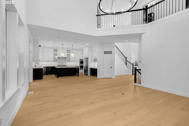 unfurnished living room with a towering ceiling, a chandelier, sink, and light wood-type flooring