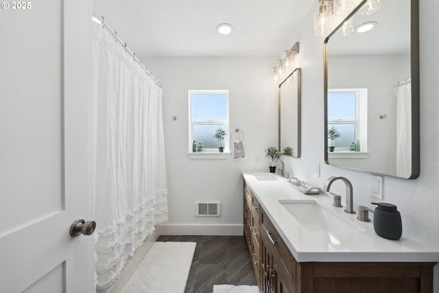 full bathroom featuring healthy amount of natural light, baseboards, and double vanity