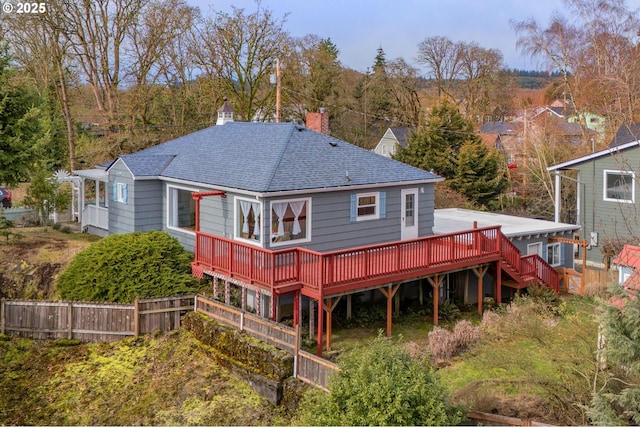 rear view of house with a shingled roof, a chimney, stairs, fence, and a deck