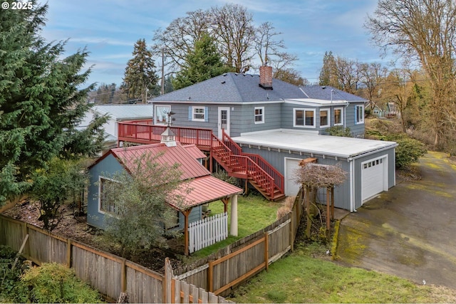 rear view of house featuring an attached garage, fence private yard, stairs, a wooden deck, and a chimney