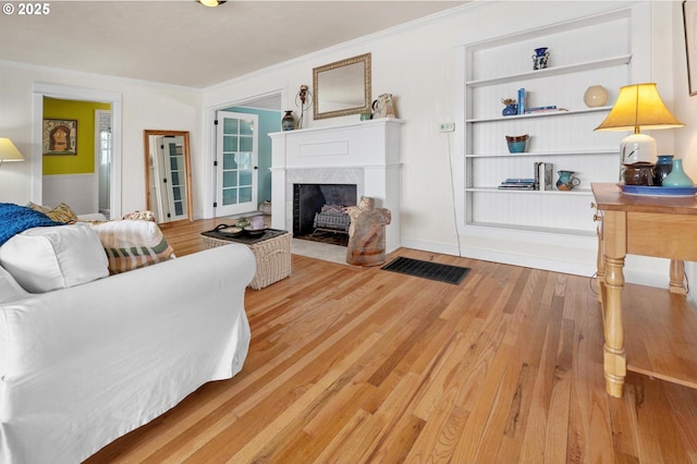 living area featuring built in shelves, wood finished floors, a high end fireplace, and crown molding