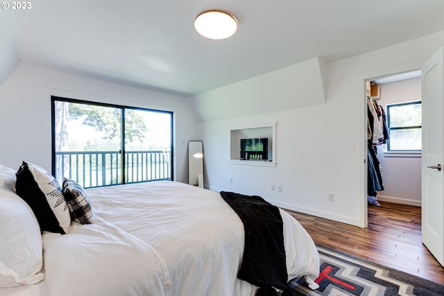 bedroom with multiple windows, wood finished floors, access to exterior, and vaulted ceiling