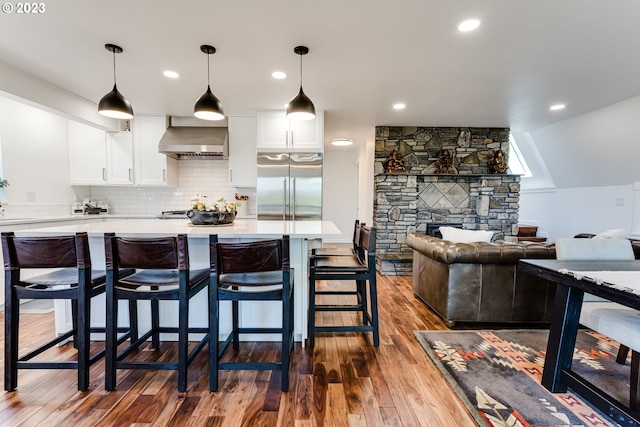 kitchen with wall chimney range hood, dark wood-style floors, built in fridge, white cabinets, and light countertops