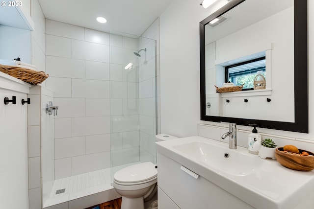 bathroom with visible vents, toilet, vanity, and a tile shower