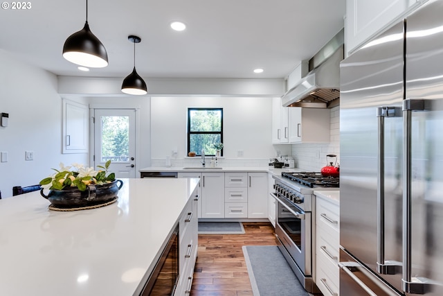 kitchen with a sink, light countertops, white cabinets, wall chimney range hood, and premium appliances