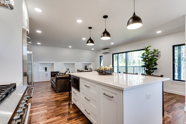 kitchen featuring dark wood-type flooring, a wall mounted air conditioner, white cabinetry, stainless steel microwave, and open floor plan