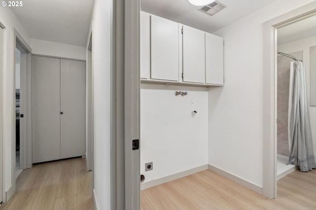 laundry area featuring visible vents, baseboards, cabinet space, electric dryer hookup, and light wood-style flooring