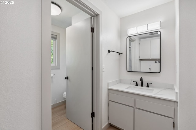 bathroom with toilet, baseboards, wood finished floors, and vanity