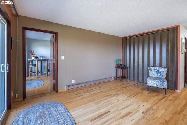 unfurnished room with baseboard heating, wood finished floors, and a textured ceiling