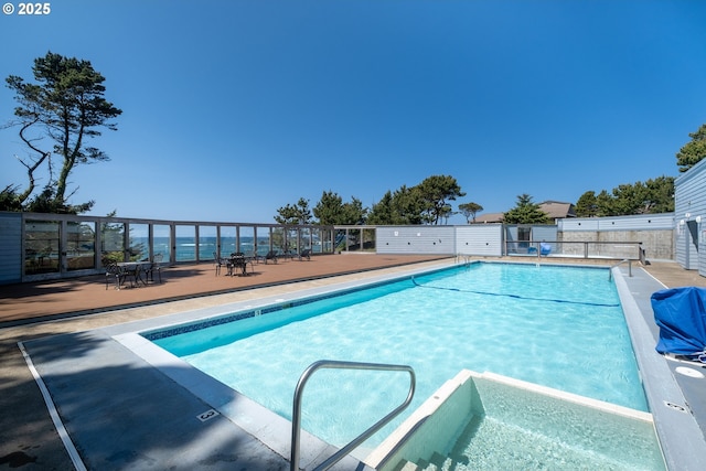 view of swimming pool featuring a pool with connected hot tub and fence