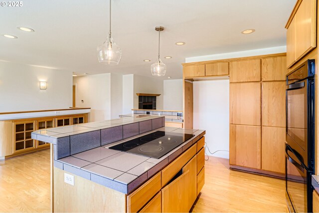 7471 SW Woodbury Loop, Wilsonville, OR 97070 - kitchen with black electric stovetop, tile counters, light wood-type flooring, a kitchen island, and recessed lighting
