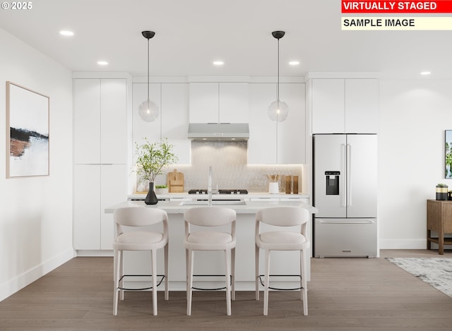 kitchen featuring light countertops, built in refrigerator, modern cabinets, under cabinet range hood, and a kitchen island with sink