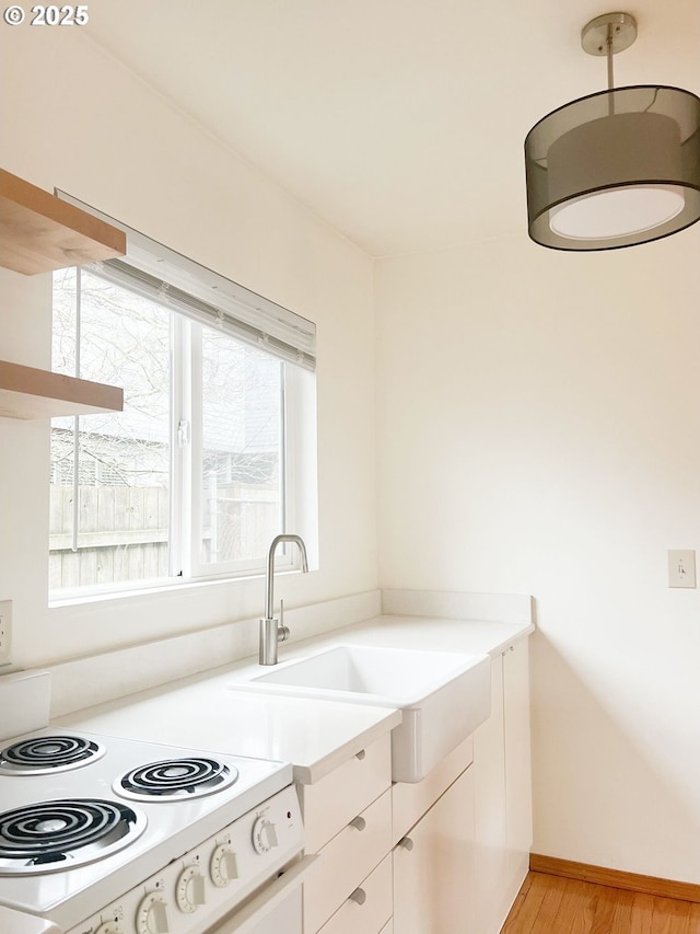 kitchen with light wood-type flooring, light countertops, white cabinets, white electric stove, and a sink