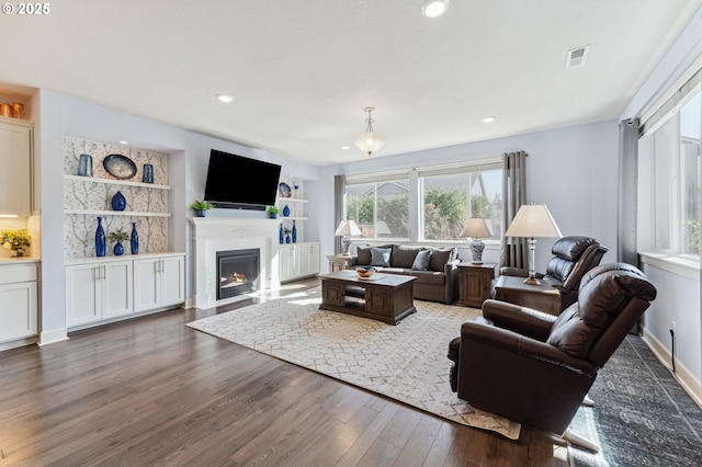 living area featuring recessed lighting, wood finished floors, visible vents, baseboards, and a glass covered fireplace