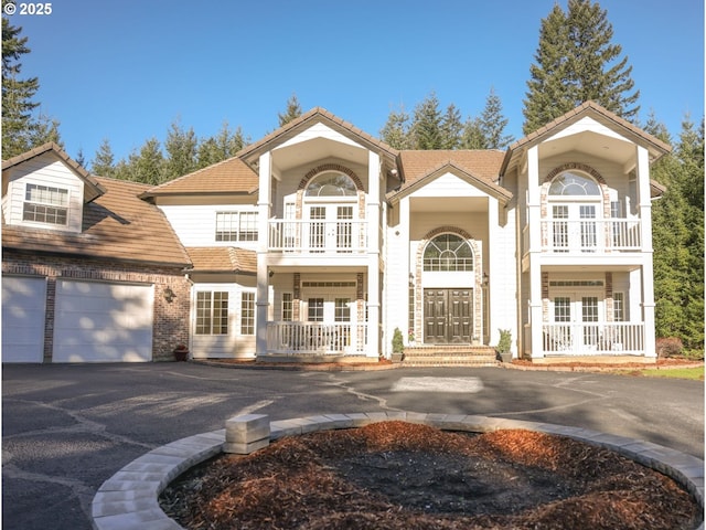 view of front of property with driveway, a balcony, covered porch, french doors, and brick siding