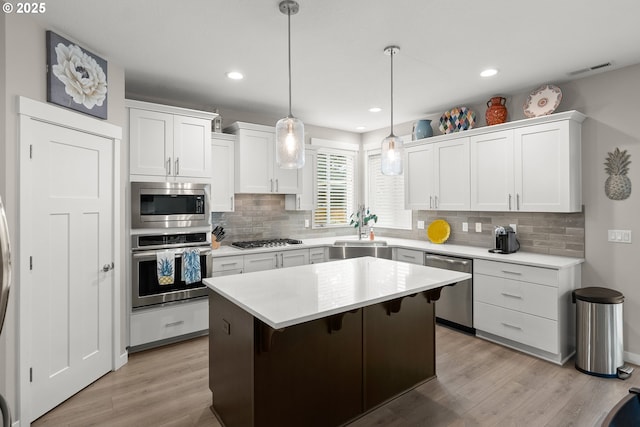 kitchen featuring a kitchen island, appliances with stainless steel finishes, white cabinetry, sink, and hanging light fixtures