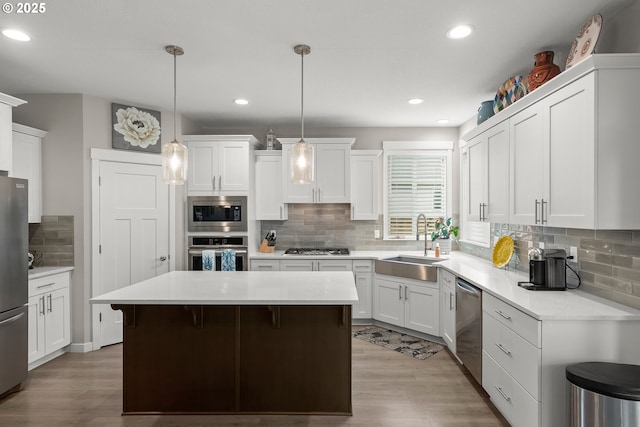 kitchen with sink, white cabinetry, hanging light fixtures, appliances with stainless steel finishes, and a kitchen island