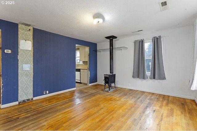 spare room featuring visible vents, a wood stove, a textured ceiling, wood finished floors, and baseboards