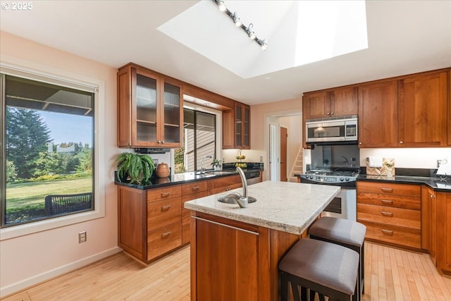 31430 NE Canter Ln, Sherwood, OR 97140 - kitchen with stainless steel appliances, light wood-type flooring, brown cabinetry, a center island with sink, and glass insert cabinets
