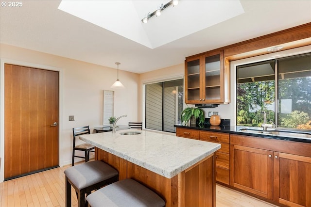 31430 NE Canter Ln, Sherwood, OR 97140 - kitchen with brown cabinets, light wood-style flooring, light stone countertops, glass insert cabinets, and a center island with sink