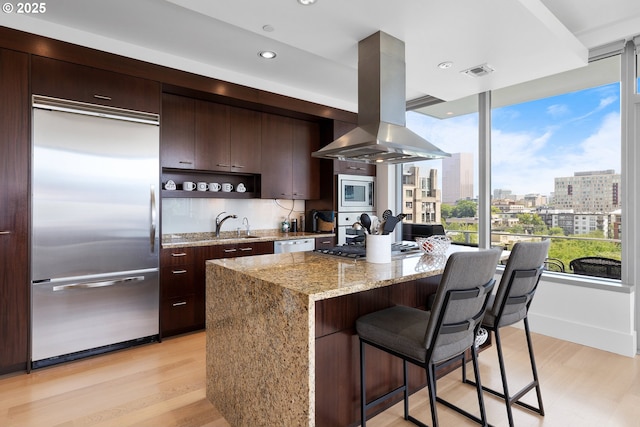 1001 NW Lovejoy St Unit 710, Portland, OR 97209 - kitchen featuring built in appliances, island exhaust hood, a kitchen island, light wood finished floors, and a breakfast bar