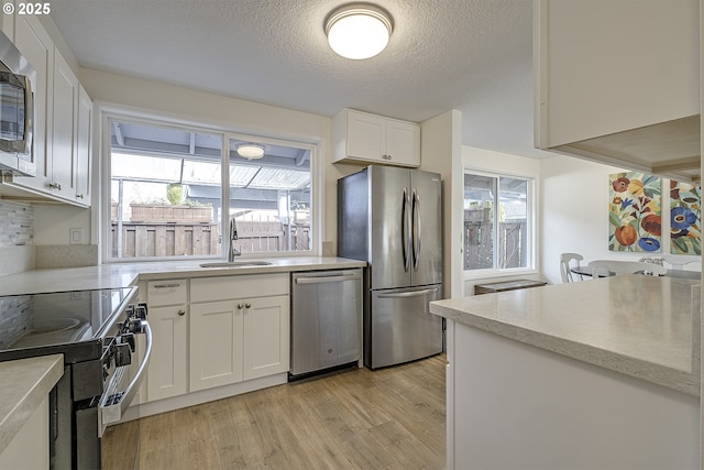 kitchen featuring white cabinetry, sink, stainless steel appliances, a textured ceiling, and light hardwood / wood-style flooring