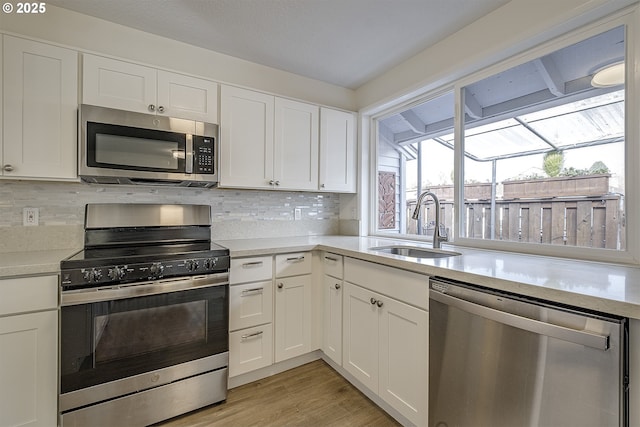 kitchen with sink, white cabinets, backsplash, light hardwood / wood-style floors, and stainless steel appliances