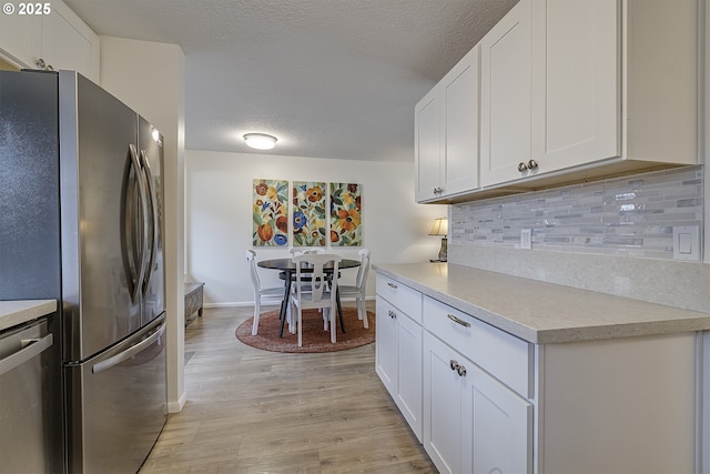 kitchen with appliances with stainless steel finishes, white cabinets, light hardwood / wood-style floors, and decorative backsplash