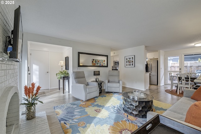 living room with a brick fireplace, light hardwood / wood-style floors, and a textured ceiling