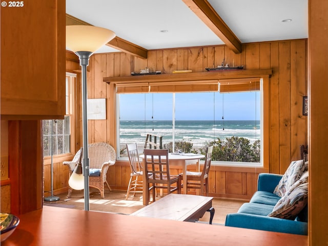 living area with wooden walls, healthy amount of natural light, beamed ceiling, wood finished floors, and a water view
