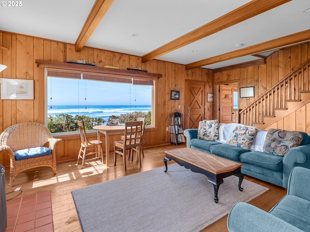 living area featuring beam ceiling, wooden walls, wood finished floors, and stairs