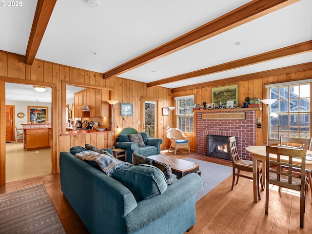 living area with beam ceiling, light wood finished floors, a brick fireplace, and wood walls