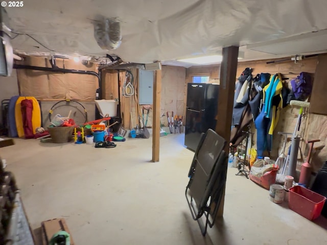 unfinished basement featuring freestanding refrigerator and electric panel
