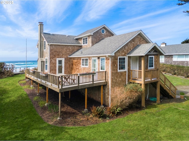 back of property featuring a chimney, a shingled roof, a deck with water view, and a yard