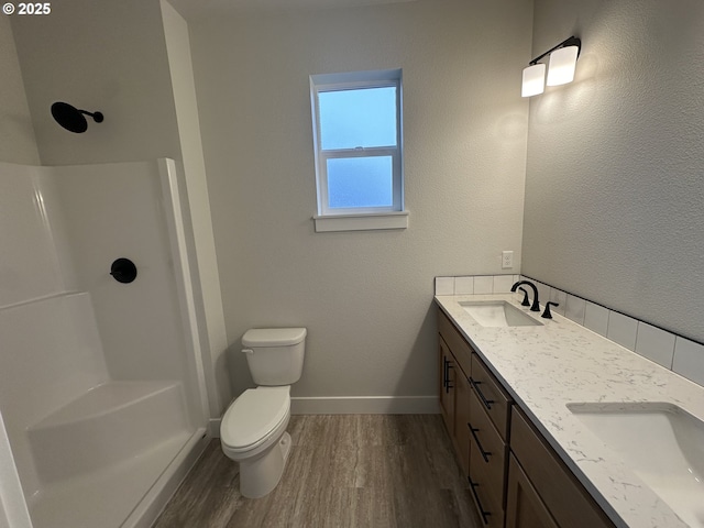 bathroom with double vanity, wood finished floors, a shower, and a sink