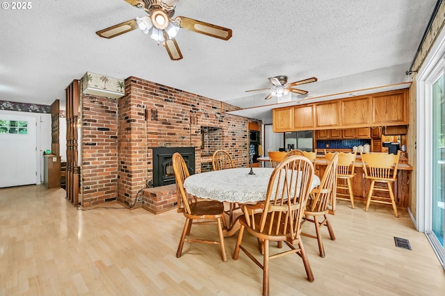 32739 Taylor Butte Rd, Cottage Grove, OR 97424 - dining area featuring ceiling fan, a textured ceiling, light wood-style floors, brick wall, and a brick fireplace
