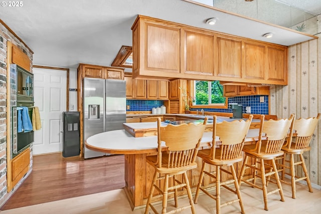 32739 Taylor Butte Rd, Cottage Grove, OR 97424 - kitchen featuring stainless steel fridge with ice dispenser, black oven, decorative backsplash, light wood-style flooring, and a breakfast bar