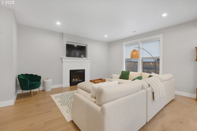 living area with baseboards, light wood-type flooring, a glass covered fireplace, and recessed lighting