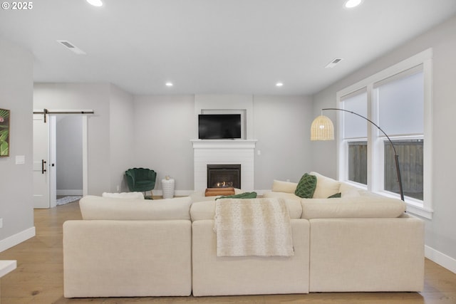 living area with recessed lighting, a barn door, a glass covered fireplace, wood finished floors, and baseboards