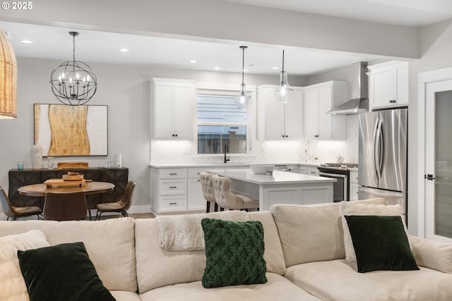 kitchen with white cabinets, open floor plan, appliances with stainless steel finishes, wall chimney exhaust hood, and tasteful backsplash