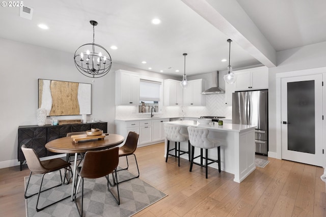 kitchen featuring light wood finished floors, tasteful backsplash, freestanding refrigerator, a kitchen island, and wall chimney exhaust hood