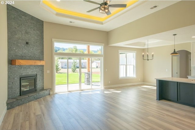 unfurnished living room with a tray ceiling, a stone fireplace, and light hardwood / wood-style floors