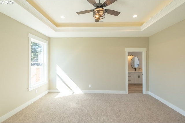 empty room featuring ceiling fan, a raised ceiling, light colored carpet, and ornamental molding