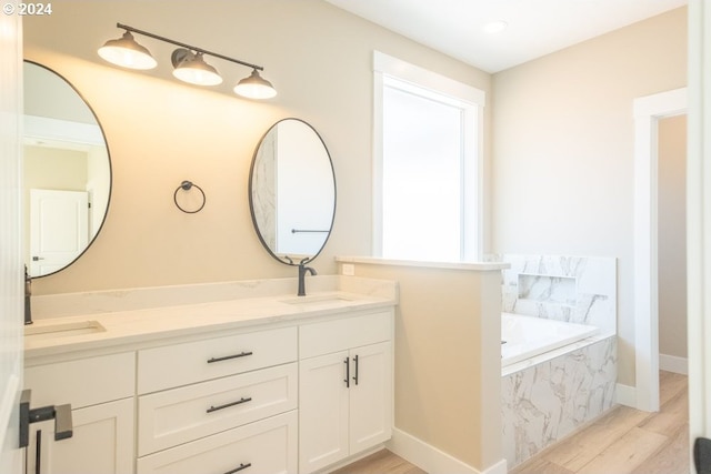 bathroom with hardwood / wood-style floors, vanity, and tiled tub