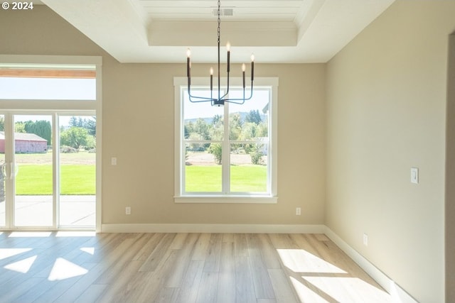 unfurnished dining area with a tray ceiling, light wood-type flooring, and a notable chandelier